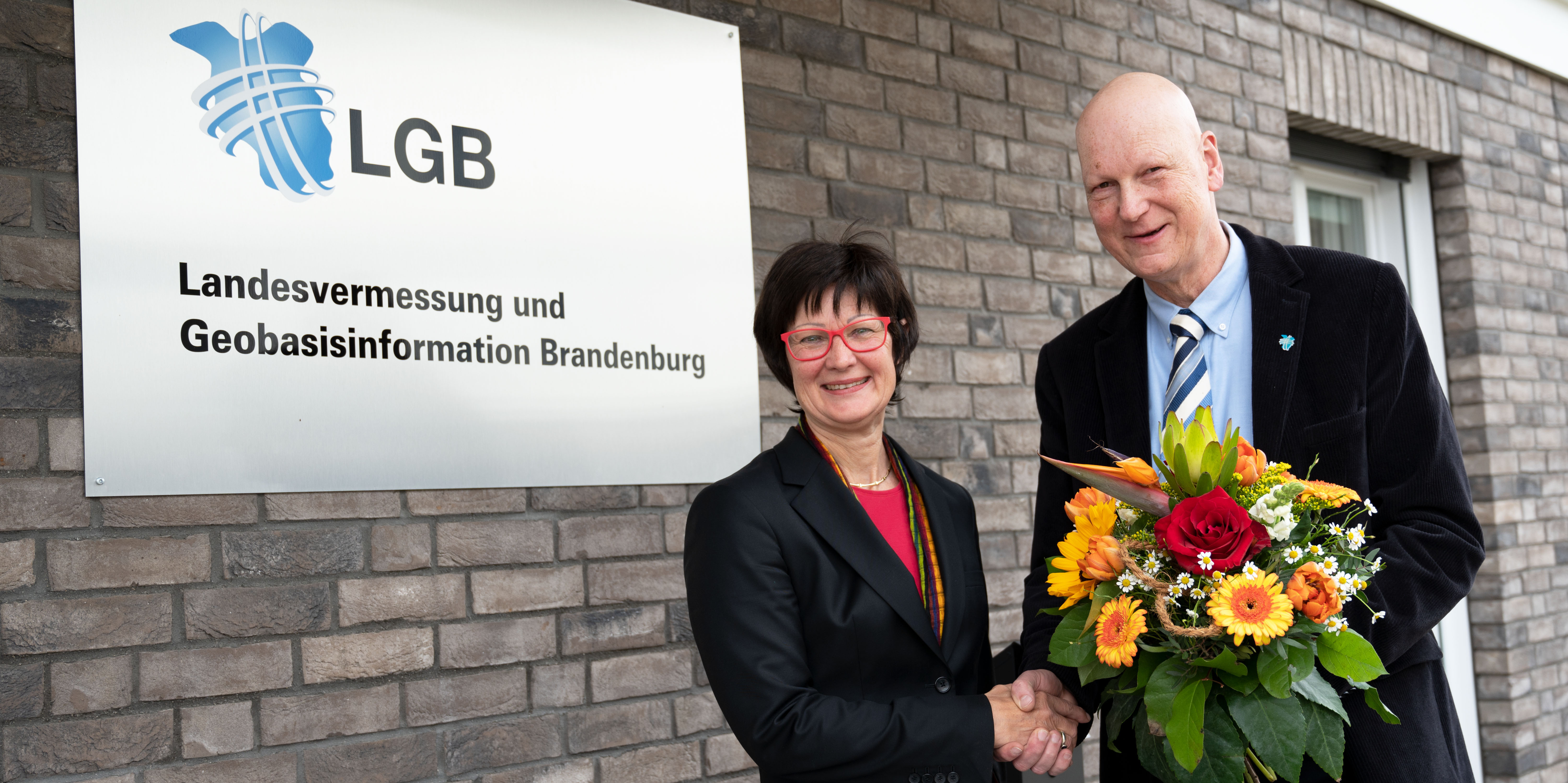 Foto vor der Betriebsstelle Potsdam der LGB: Bernd Sorge begrüßt Gisela Fabian mit einem Blumenstrauß und wünscht ihr viel Erfolg für die neue Tätigkeit.