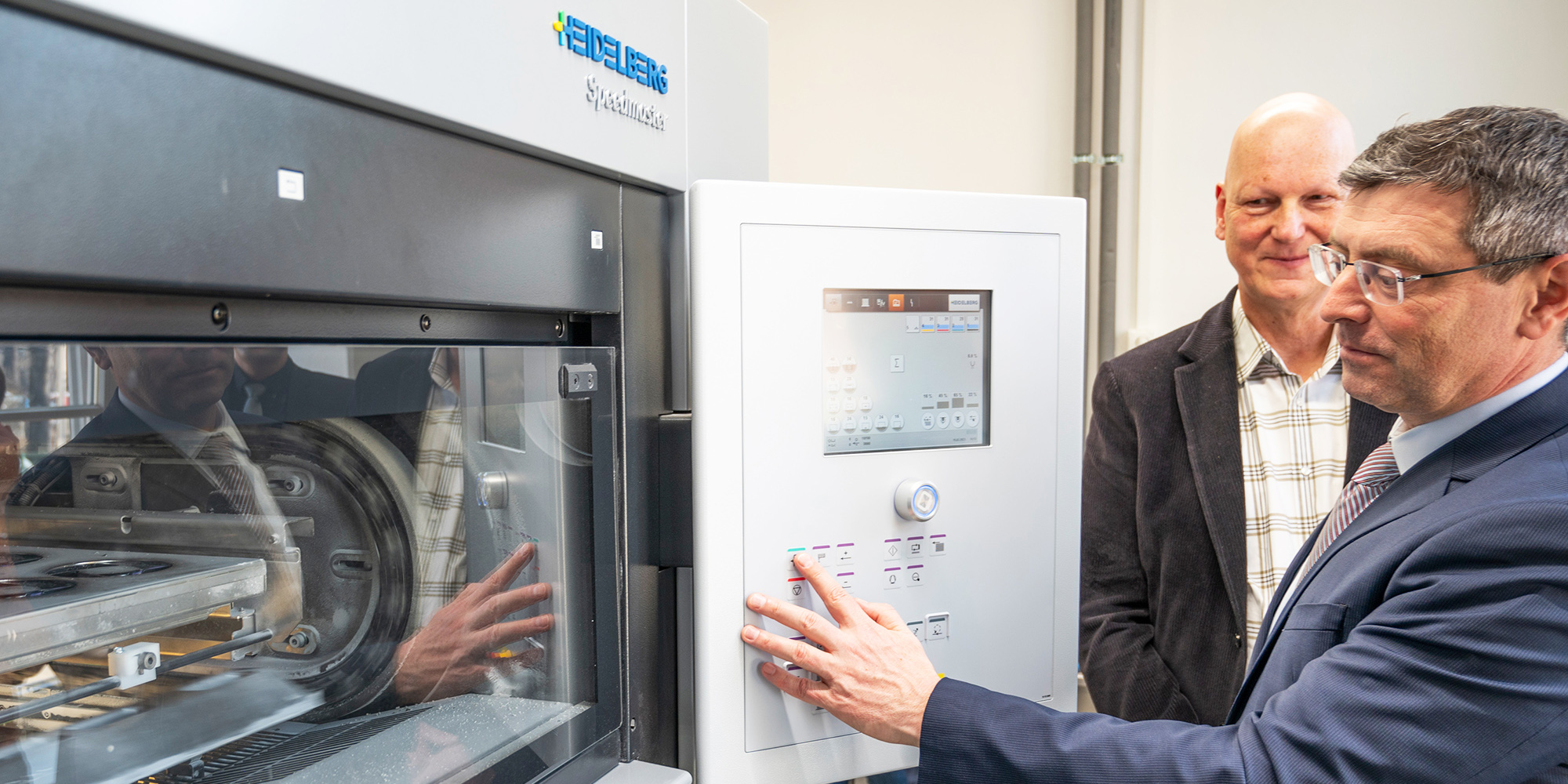 Foto von Staatssekretär Uwe Schüler (MIK) im Beisein des LGB-Geschäftsführers (i.V.) Bernd Sorge wie er symbolisch den Knopf an einer Druckmaschine betätigt